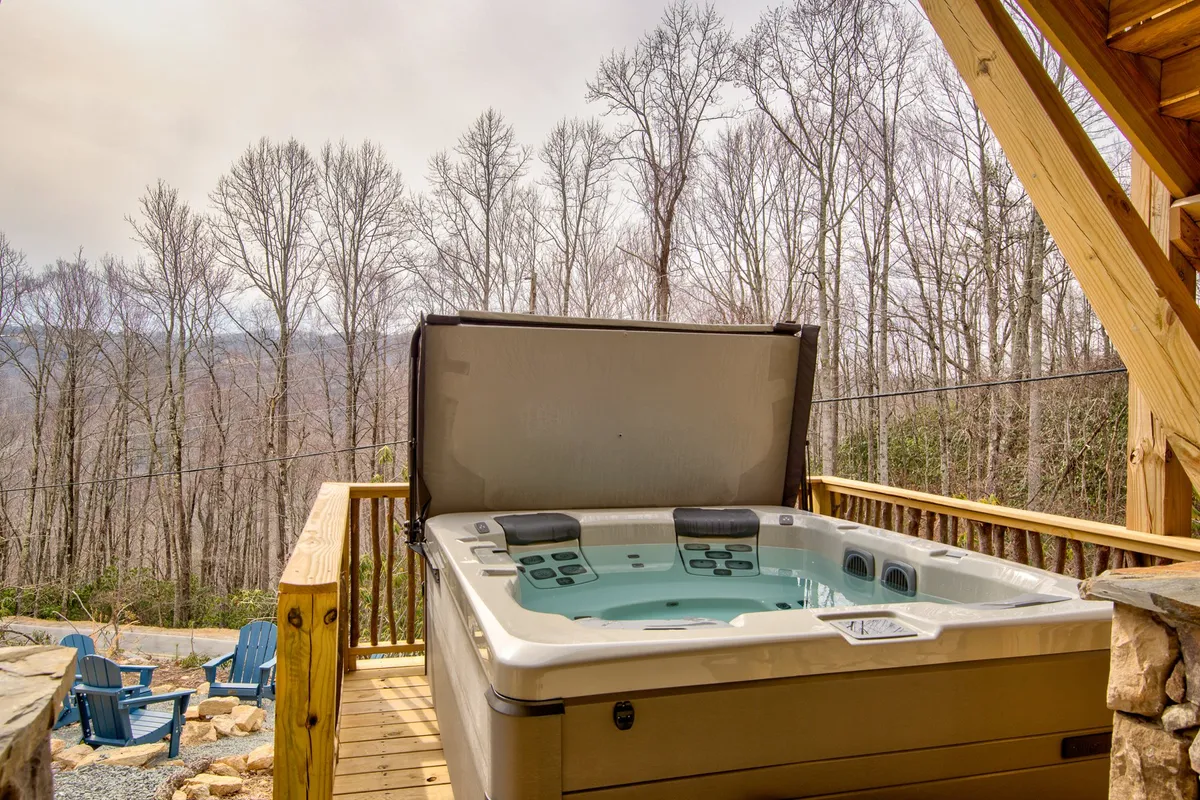 This image showcases a peaceful hot tub nestled on a wooden deck, surrounded by tall trees, offering a tranquil retreat immersed in nature. The hot tub is a focal point, while the wooden deck seamlessly blends indoor comfort with the serenity of the outdoors, hinting at the immersive mountain experience.