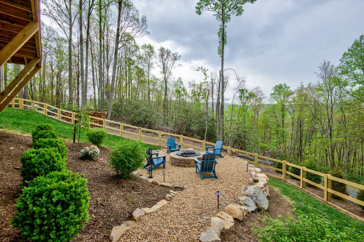 This exterior image captures a cozy fire pit surrounded by Adirondack chairs, set amidst lush greenery and a charming fence. The scene evokes a sense of warmth and togetherness, perfect for families roasting marshmallows, sharing stories, or simply relaxing under the stars.