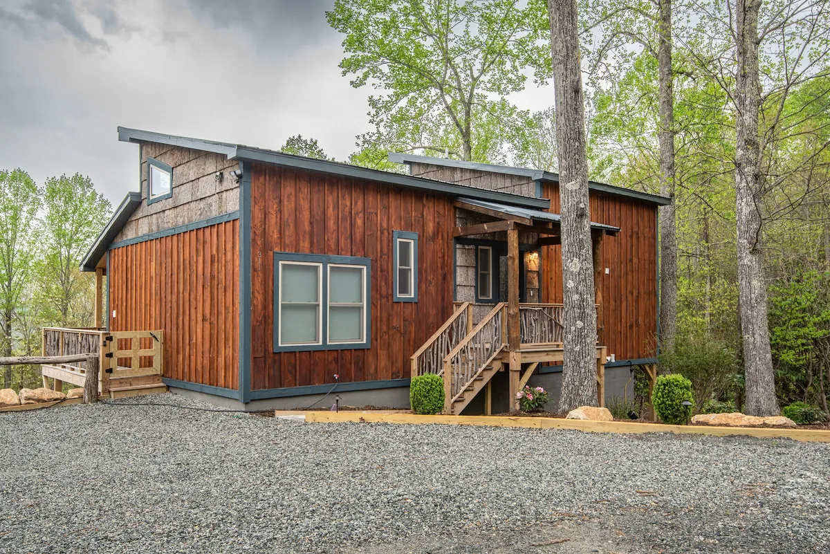 A cozy wooden exterior with a front porch and landscaped area. The porch offers a space to relax while taking in nature, with the home blending seamlessly into its environment.