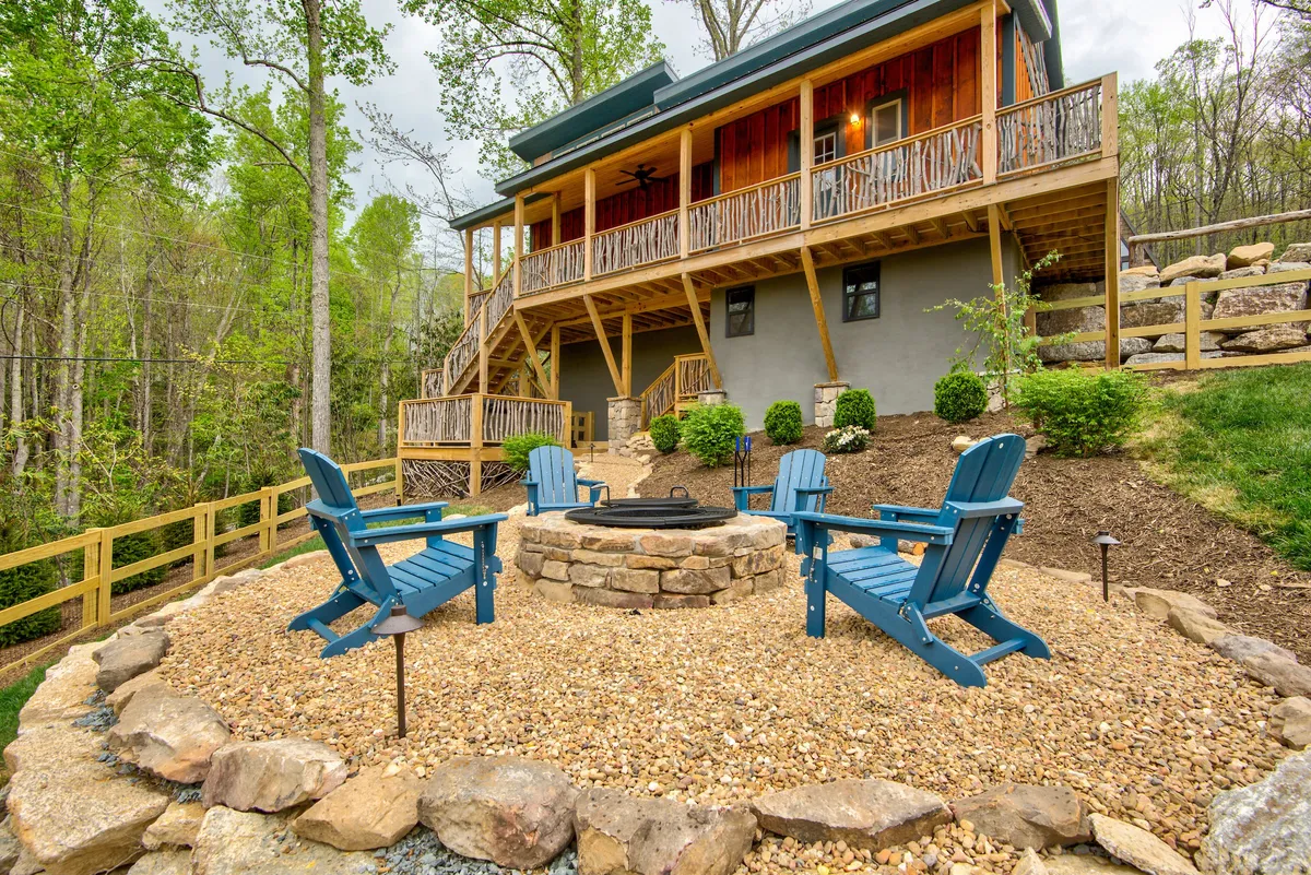 A cozy fire pit surrounded by blue Adirondack chairs sits atop a wooden deck, framed by greenery. The scene suggests gatherings around the fire, sharing stories or making s’mores under the sky, with ample space for relaxation and communal enjoyment.