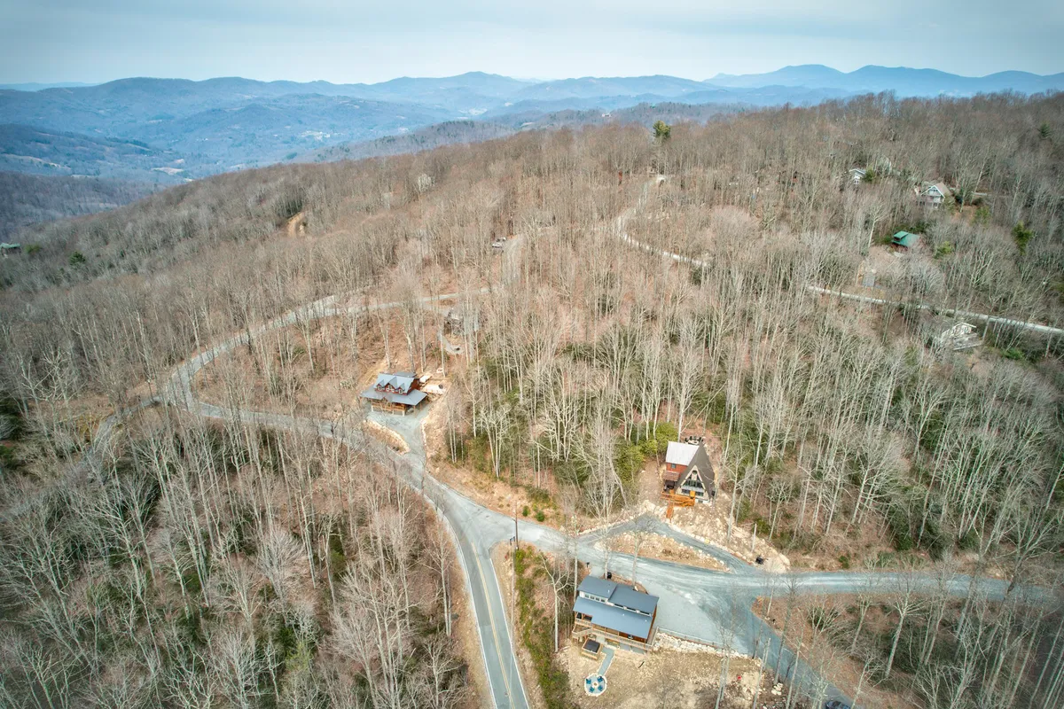 A wide view of the mountain range in the background, with scattered homes nestled among bare trees and winding roads leading through the landscape. The scenery highlights the natural beauty and adventurous terrain surrounding the area.