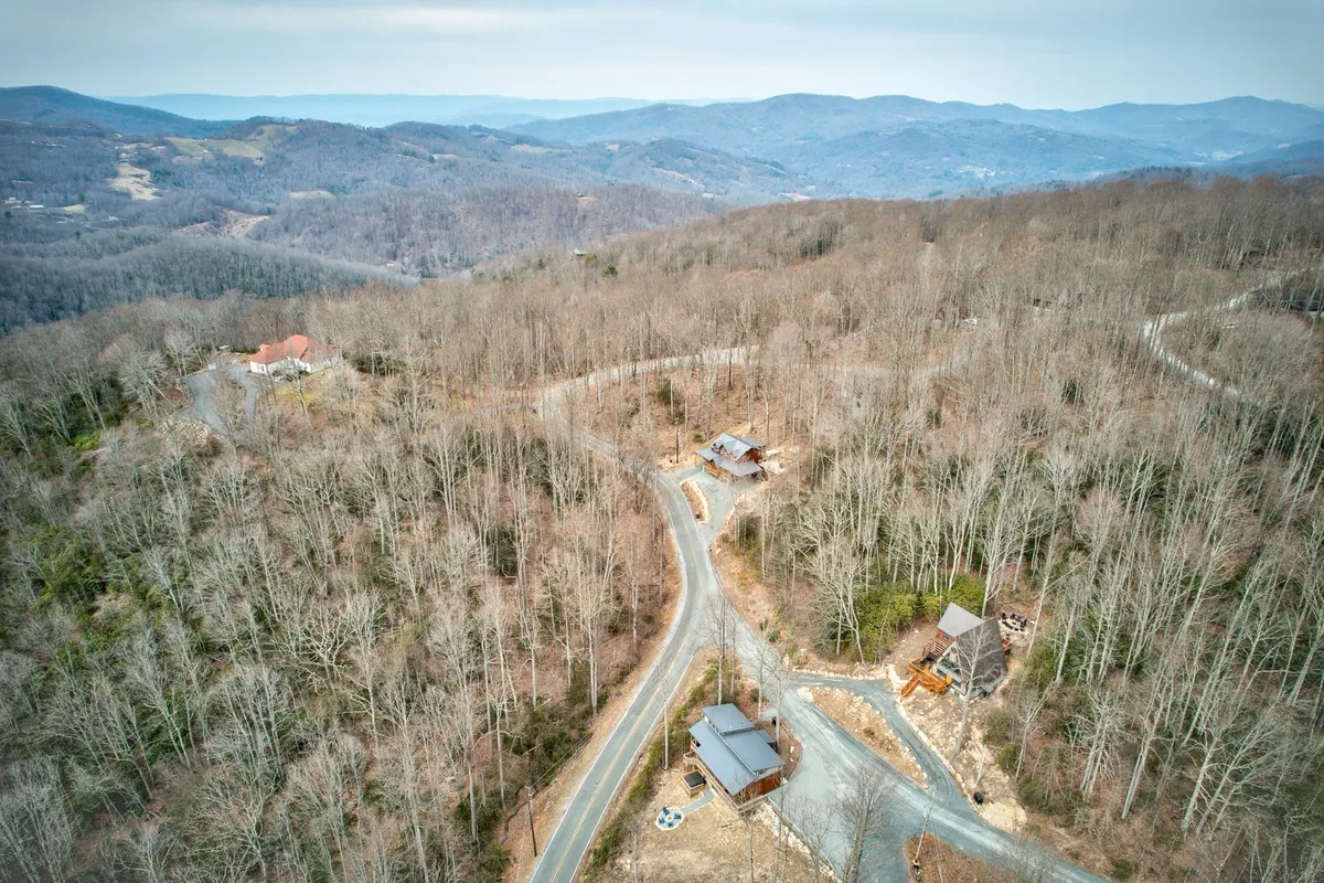A beautiful landscape of winding roads, wooded areas, scattered mountain cabins, and a breathtaking mountain range in the background. The image suggests endless opportunities for exploration, hiking, and connecting with the natural surroundings of Beech Mountain.