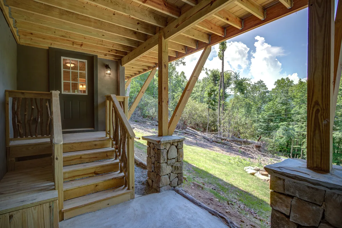 The front entrance of the home, with sturdy stone pillars and wooden stairs leading to a welcoming front porch. Surrounded by lush greenery, the scene evokes the arrival experience and hints at both comfort and the natural beauty that defines the retreat.