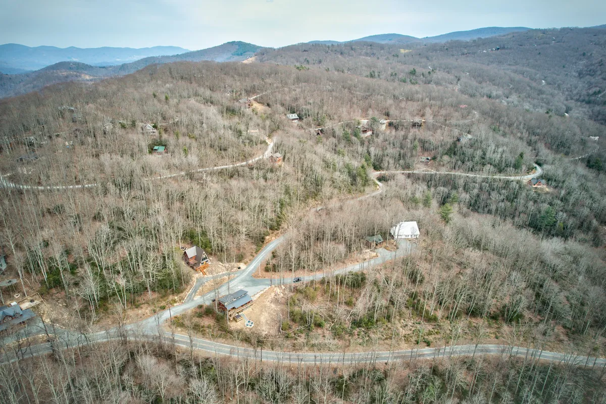 A breathtaking wide-angle view of the mountain landscape dotted with scattered cabins and winding roads. The mountains provide a dramatic backdrop, emphasizing the secluded and scenic nature of the getaway location.