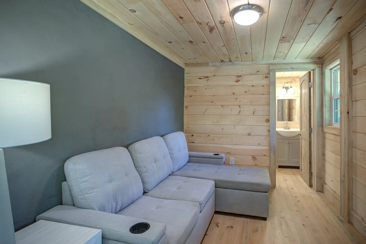 This image features a comfortable sofa positioned near a lamp and shows a doorway leading into a bathroom. The scene is cozy and welcoming, highlighting a relaxing spot that could serve as both a sitting area and sleeping space, with easy access to the private bath.