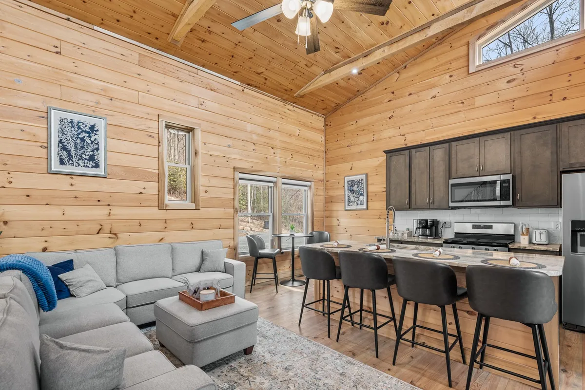 This image presents an expansive interior that seamlessly blends a sofa seating area with a visible kitchen island and an adjacent dining area. Warm wood tones, plush furnishings, and natural light create a welcoming space ideal for communal activities.